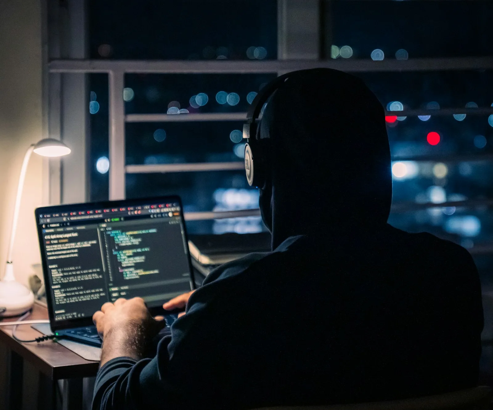 An AI developer in headphones working through code on a laptop at night.