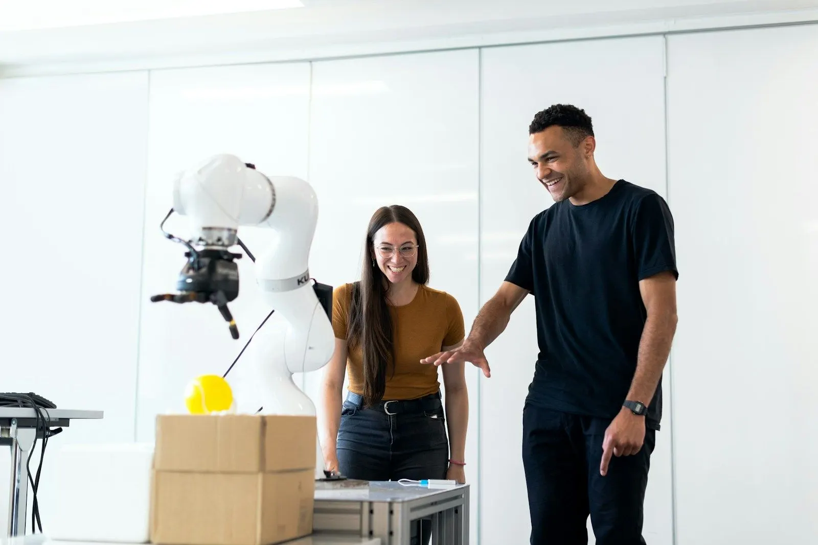 Two AI developers discussing a robot arm they are testing in a bright lab.