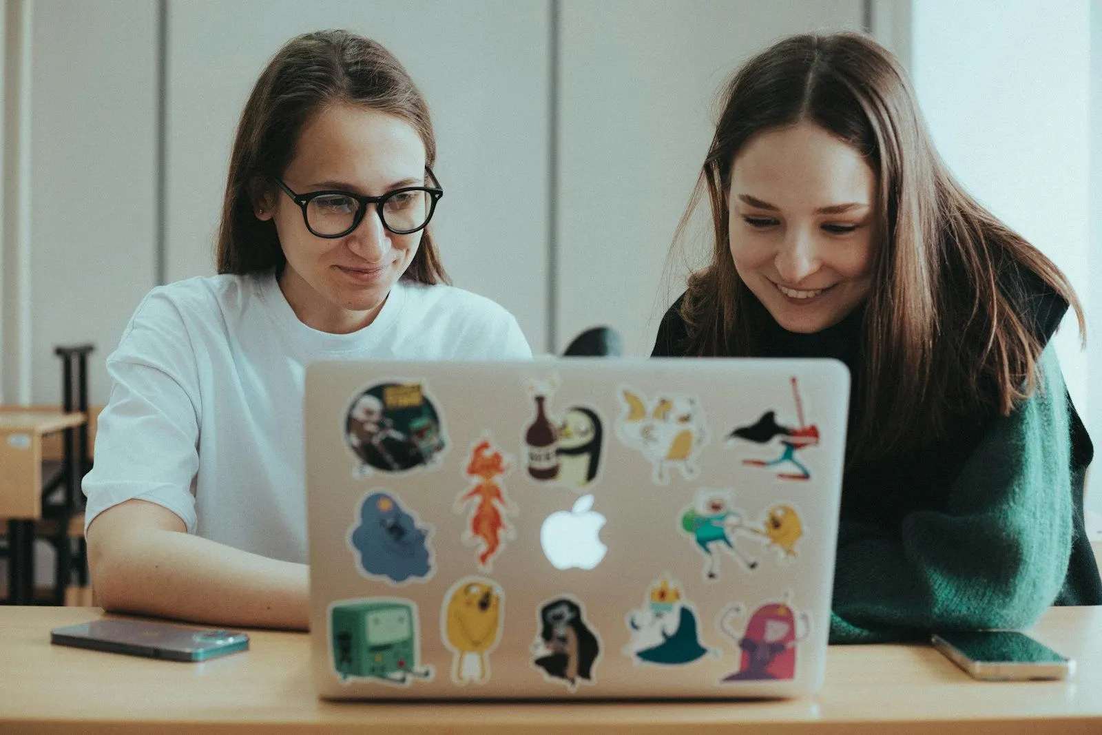 Two AI evaluation engineers working together on a sticker-covered laptop.