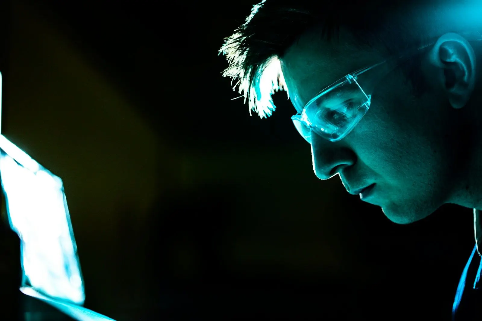An LLMOps engineer in glasses lit by the glow of a screen in a dark lab.