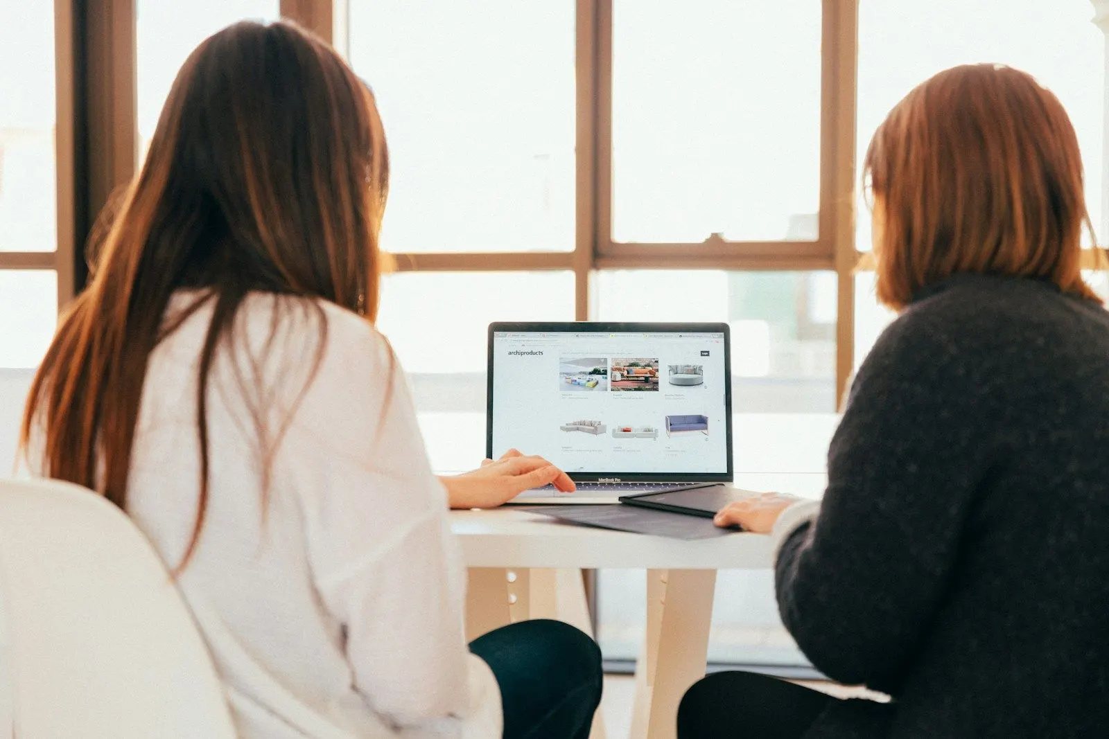 Two colleagues reviewing how to hire AI developers on a laptop by a large window.