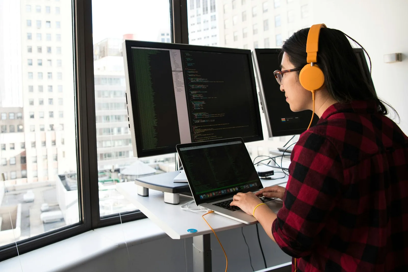 A Machine Learning developer in headphones working at a standing desk with code on two monitors.
