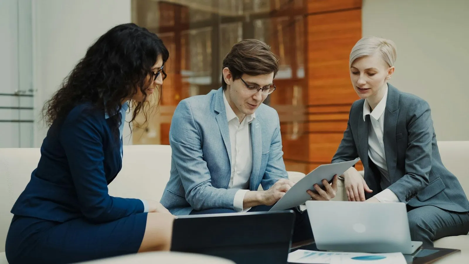 Three colleagues reviewing how to hire a Machine Learning developer on a tablet on an office sofa.