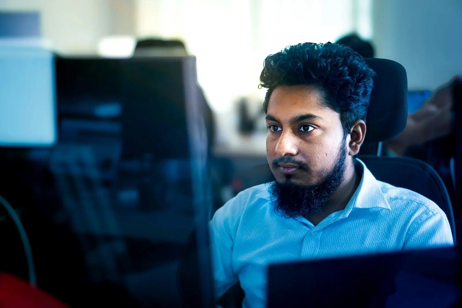 A data engineer concentrates at his screen in a busy, blue-lit office.