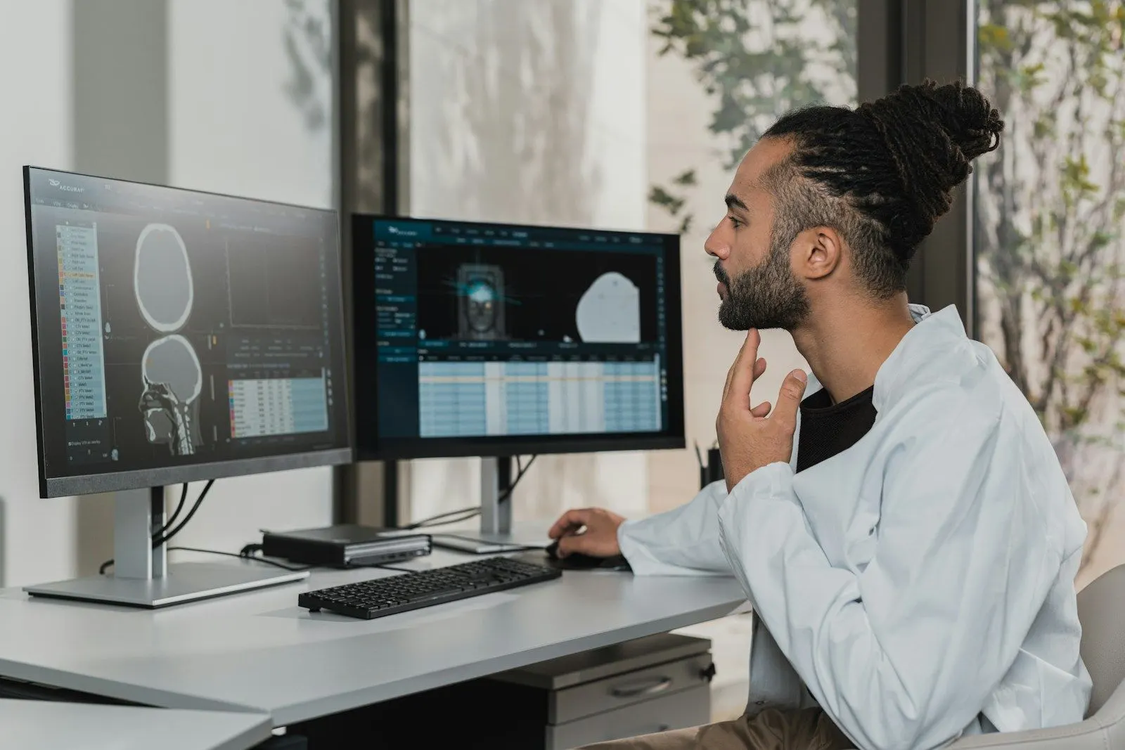 An analytics engineer with braided hair studies modelled tables on two monitors.