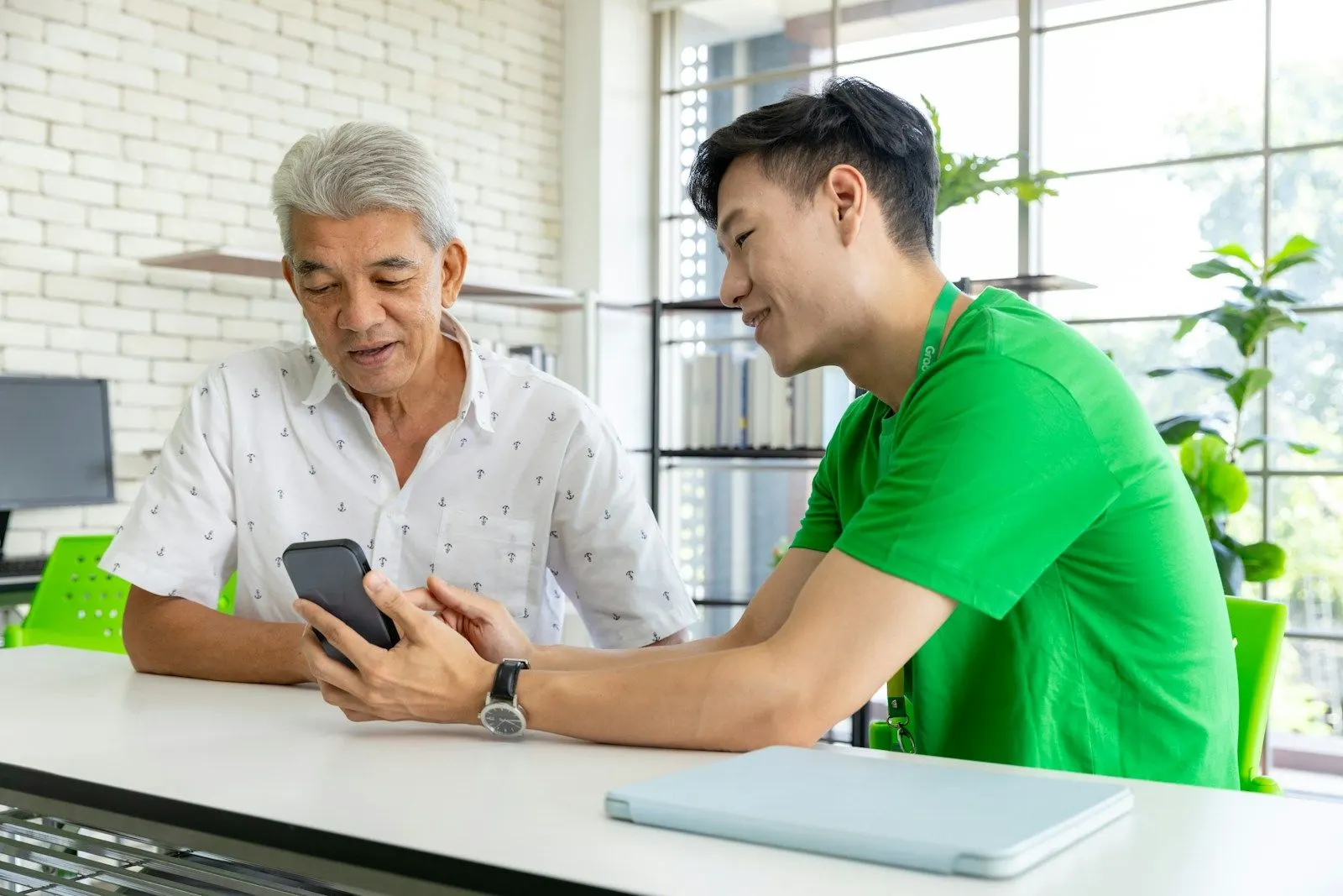 A senior UI automation engineer and a colleague check an app on a phone together at a desk.