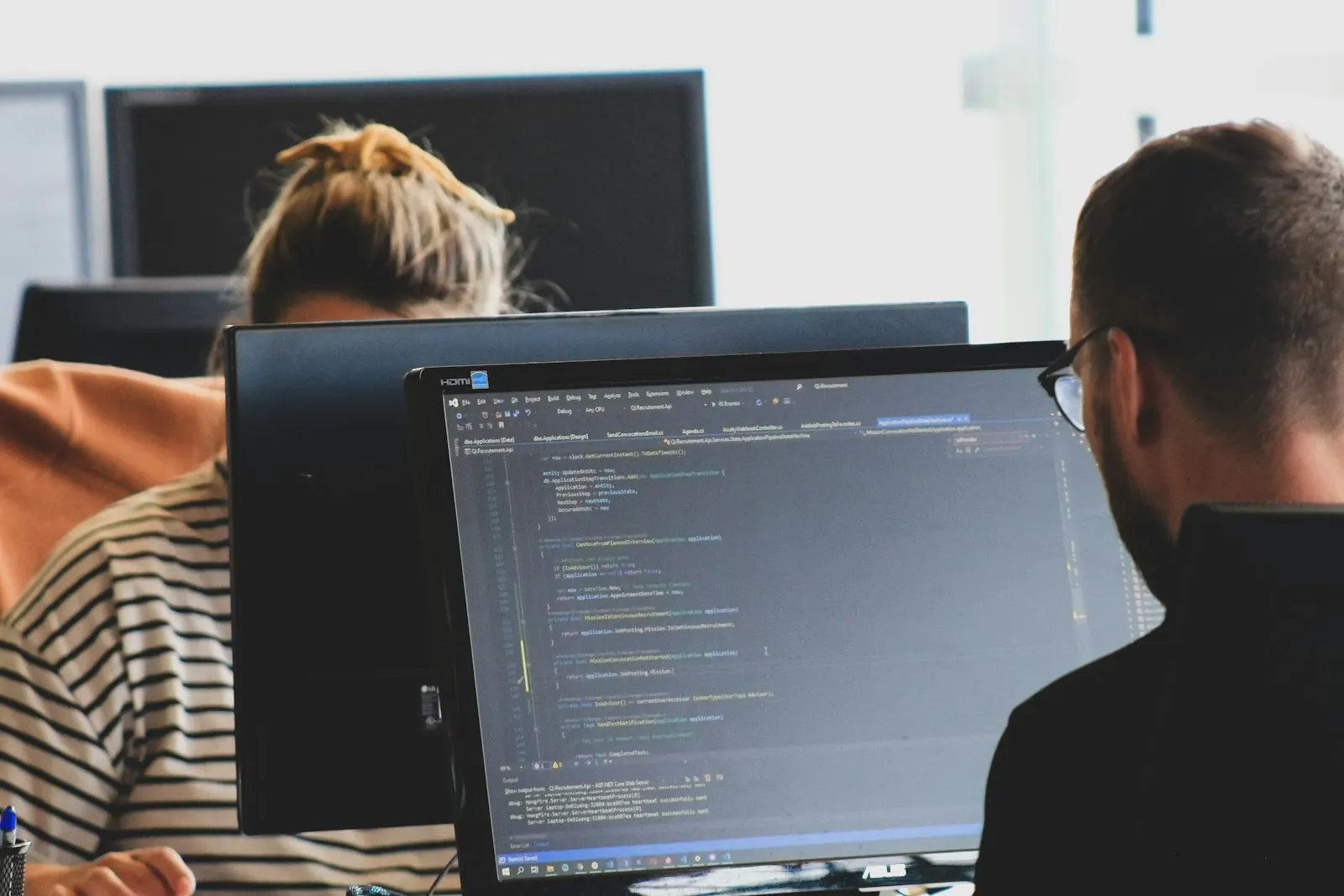 Two QA Automation Engineers work through test code at their monitors in a bright office.