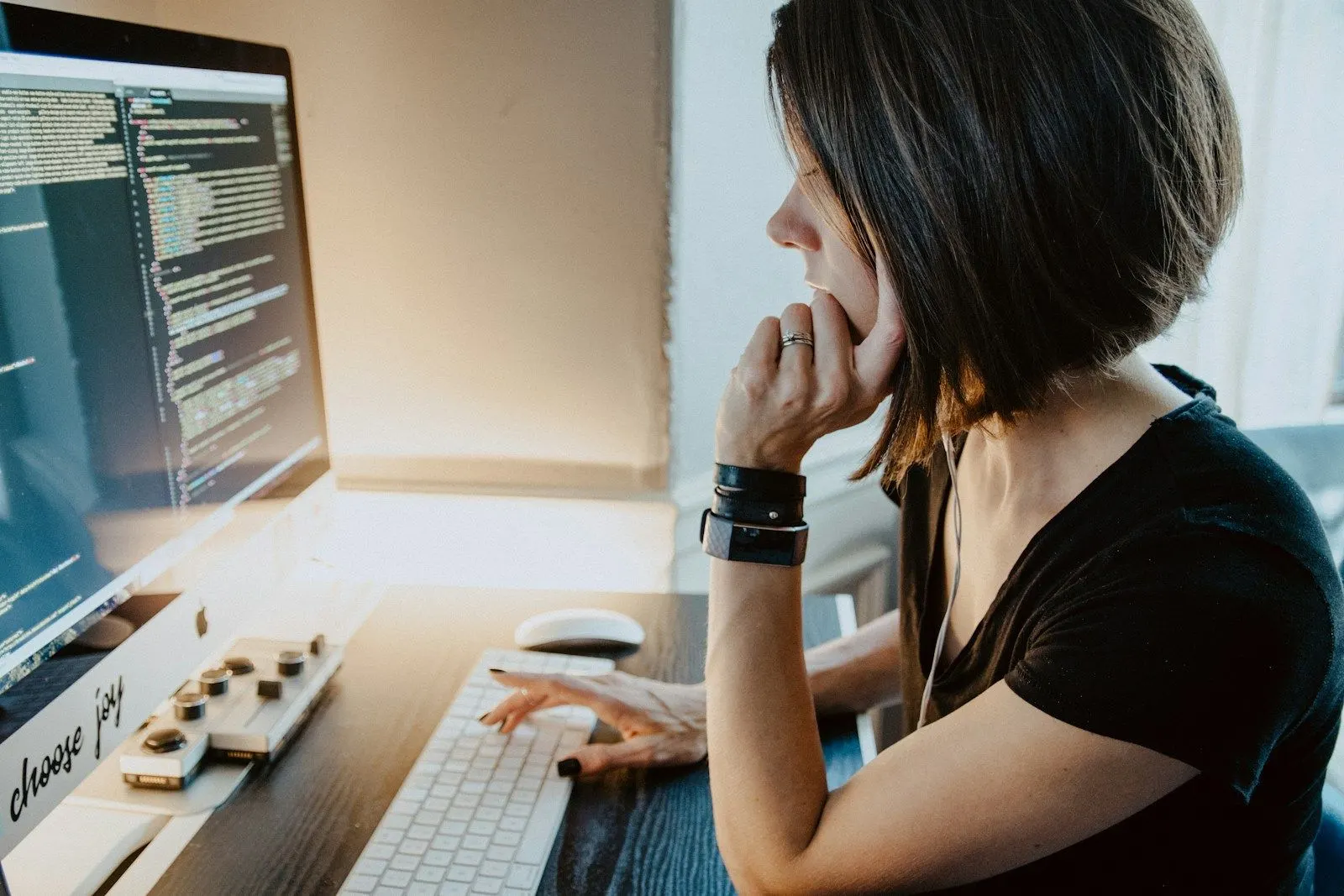 A QA Automation Engineer rests her chin on her hand as she reads test code on her monitor.