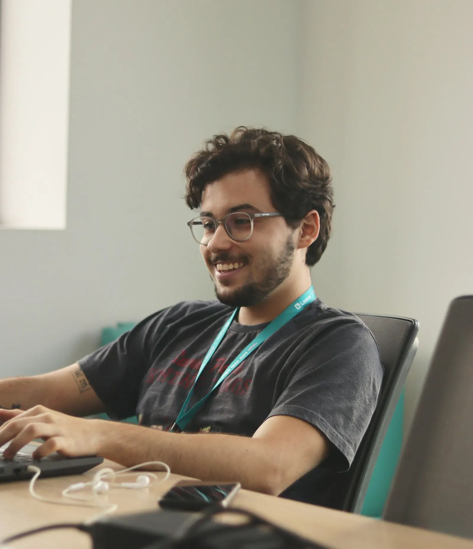 A US onshore back-end developer in glasses smiles as he types at his desk.
