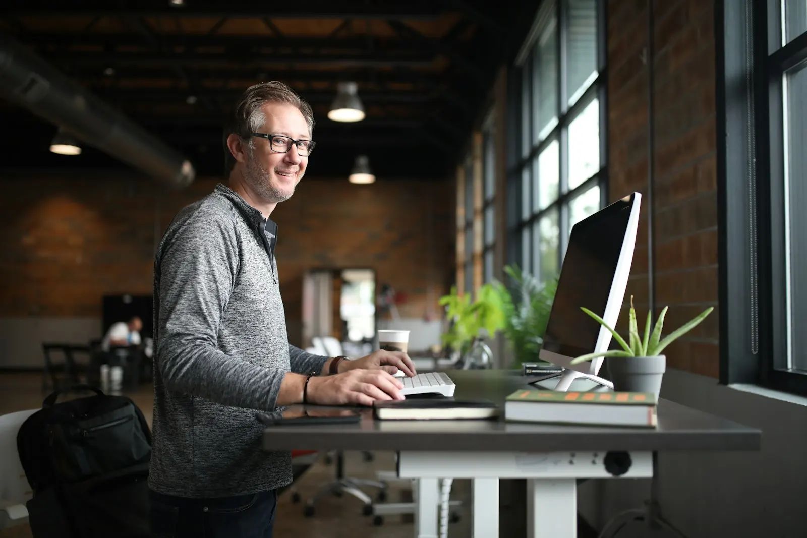 A US onshore DevOps engineer stands at a standing desk in a long, bright office.
