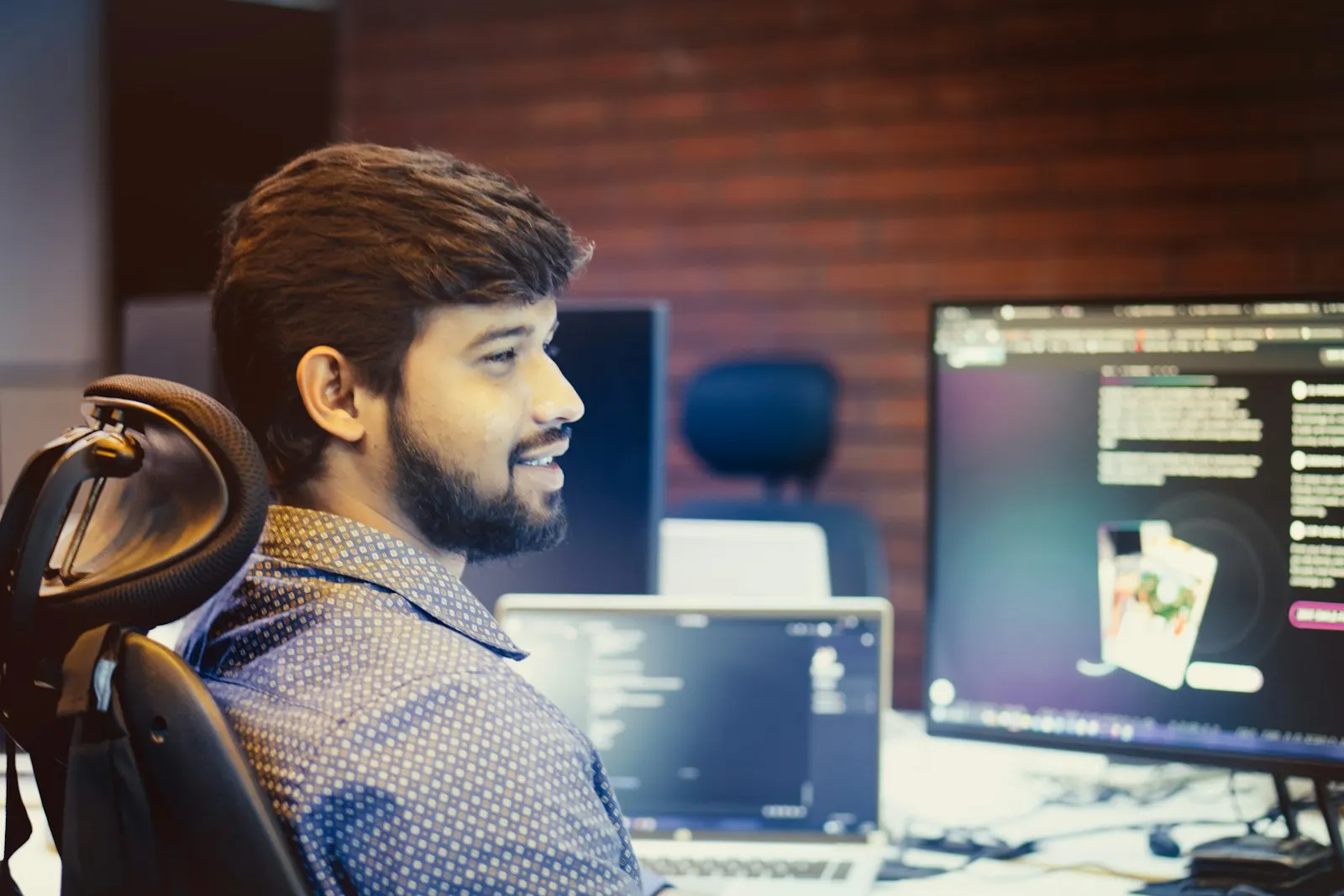 A US onshore machine learning engineer smiles at his screens in a brick-walled office.