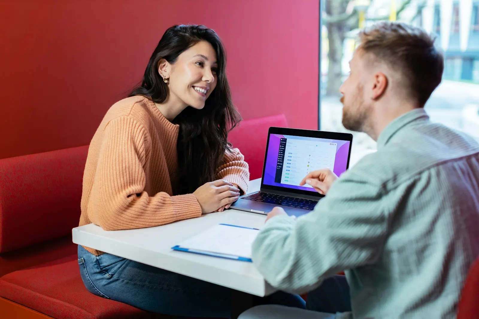Two colleagues talk over a laptop at a table.