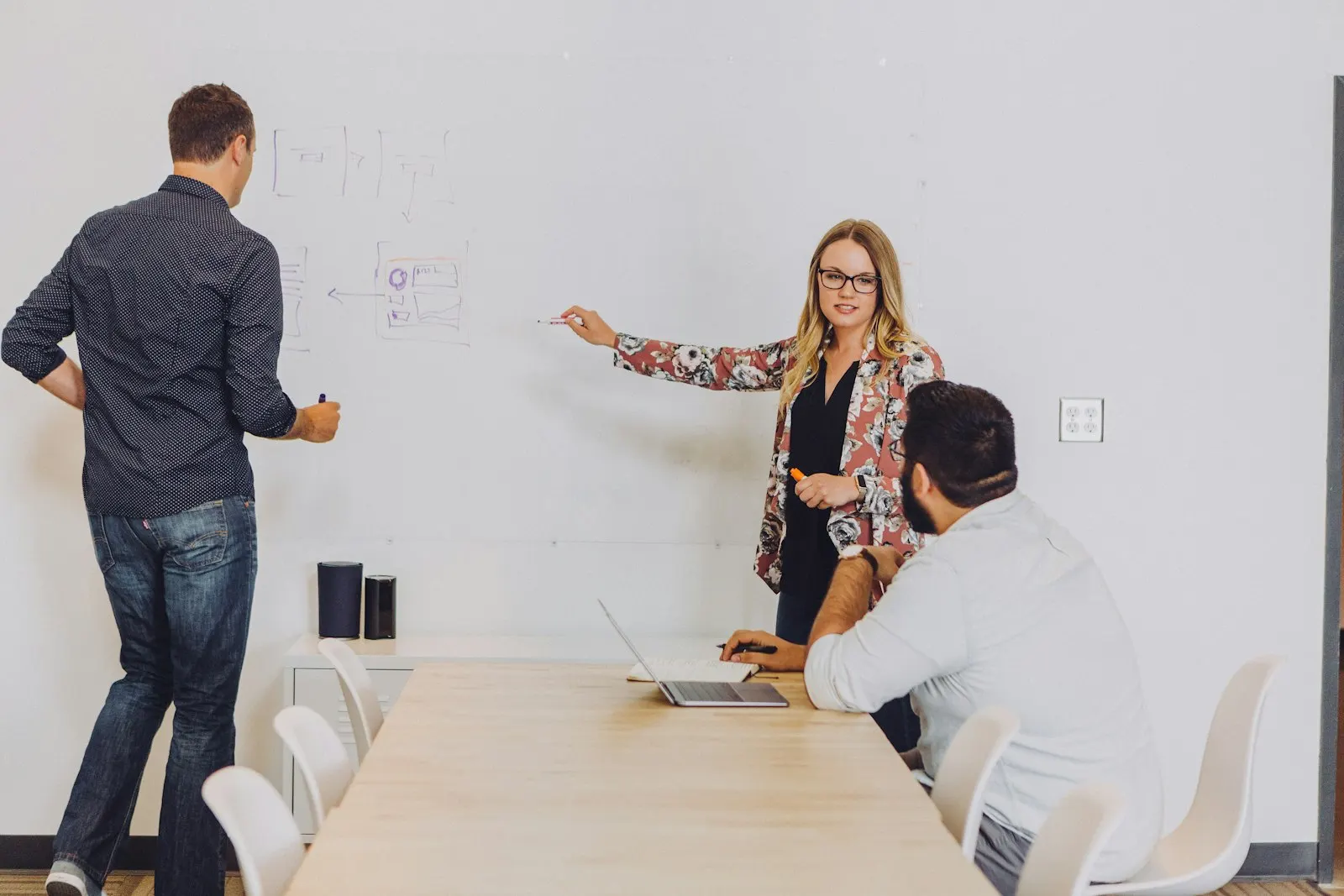 A team lead sketches options on a whiteboard with two colleagues.