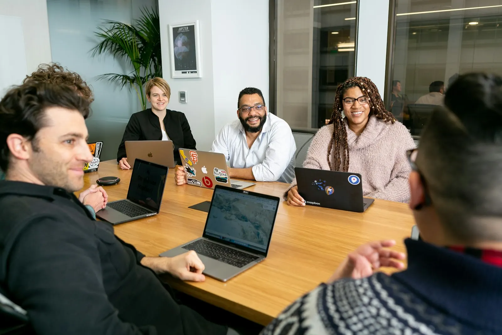 An onshore product team with laptops talks around a long table.