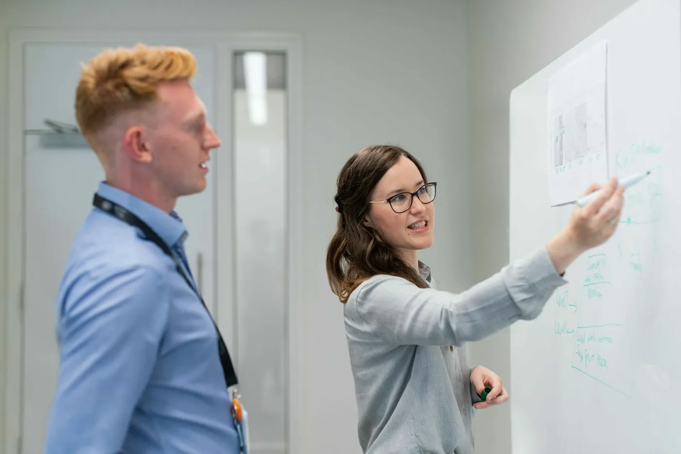 Two colleagues sketch a plan on a whiteboard.