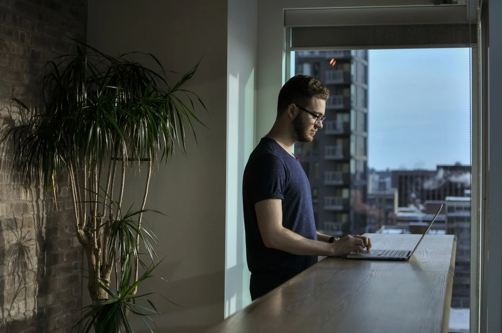 A nearshore developer in Canada works on a laptop at a counter by a tall window.