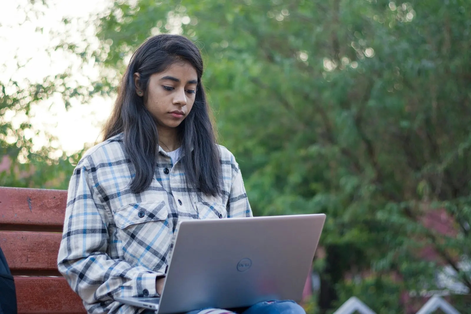 An offshore data engineer in India works on a laptop on a bench outdoors.