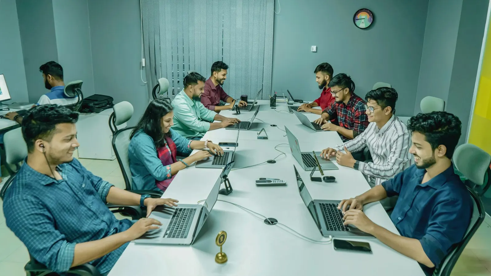 Engineers work together at laptops around a long table.