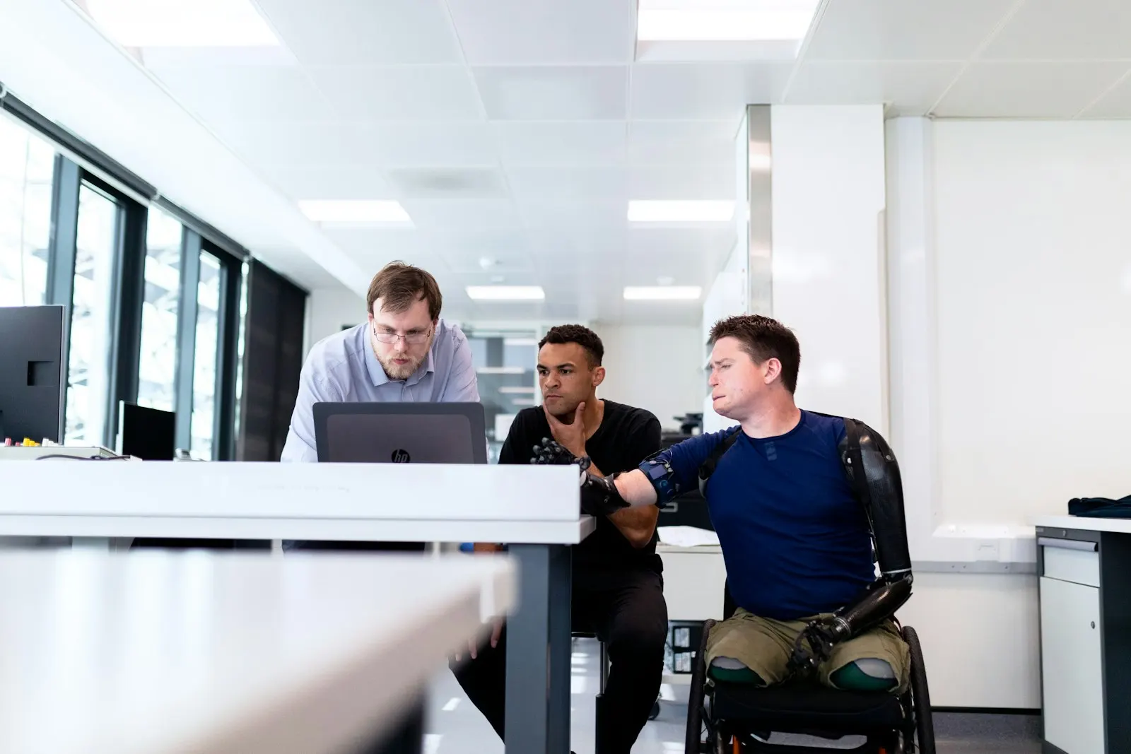 Three engineers at a global capability center in India work through a problem at one laptop.