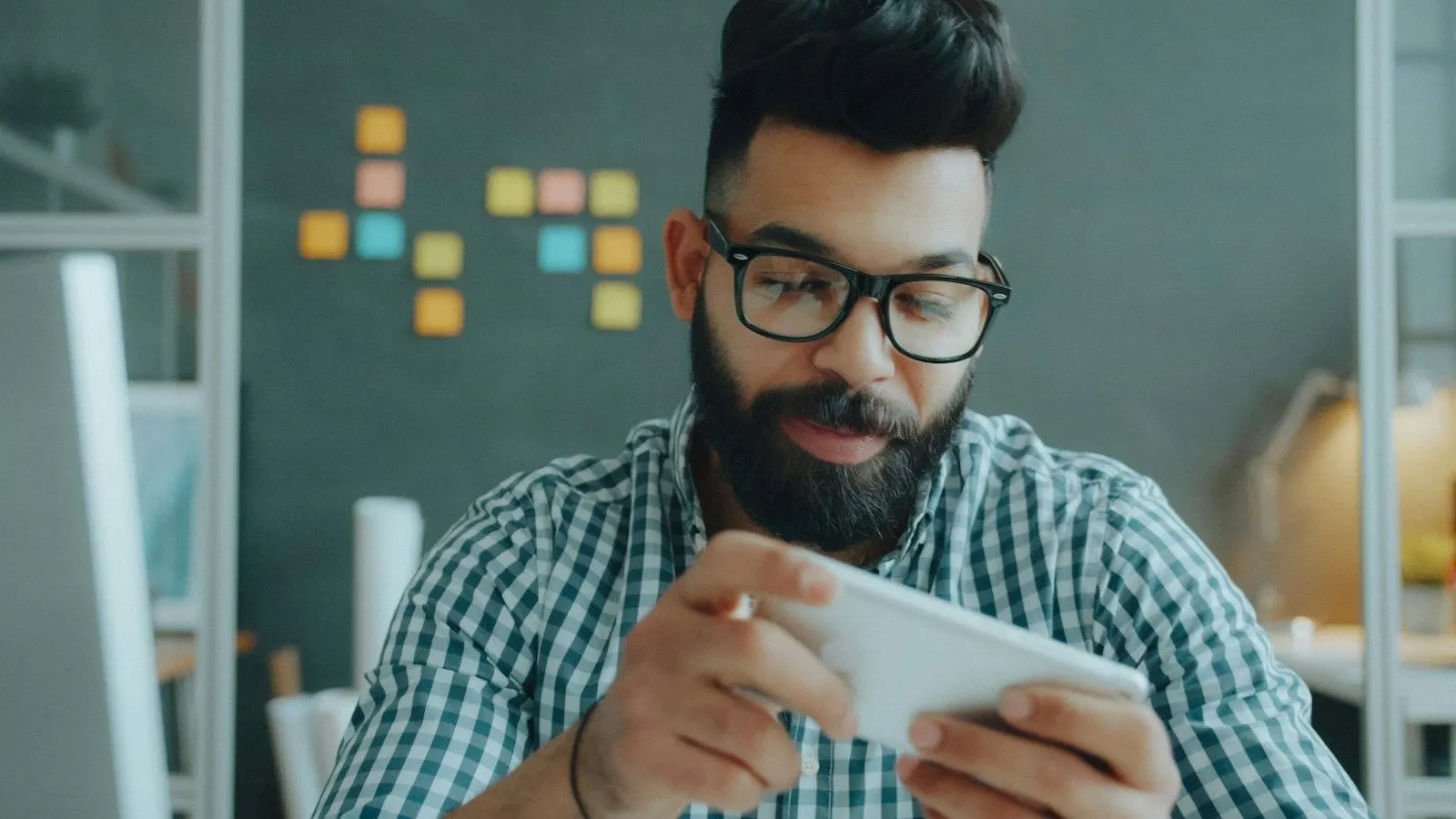 A QA lead in glasses tests an app on a phone held sideways.
