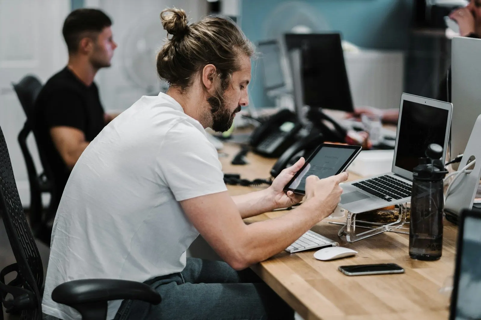 An exploratory tester checks an app on a tablet at his desk beside a laptop.