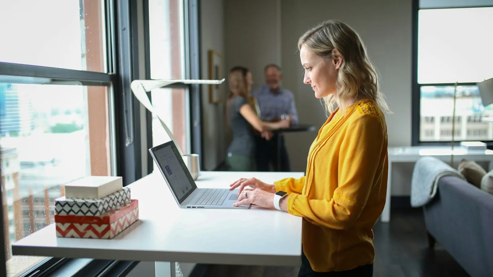 A QA engineer in a yellow sweater works through test cases on a laptop at a standing desk.