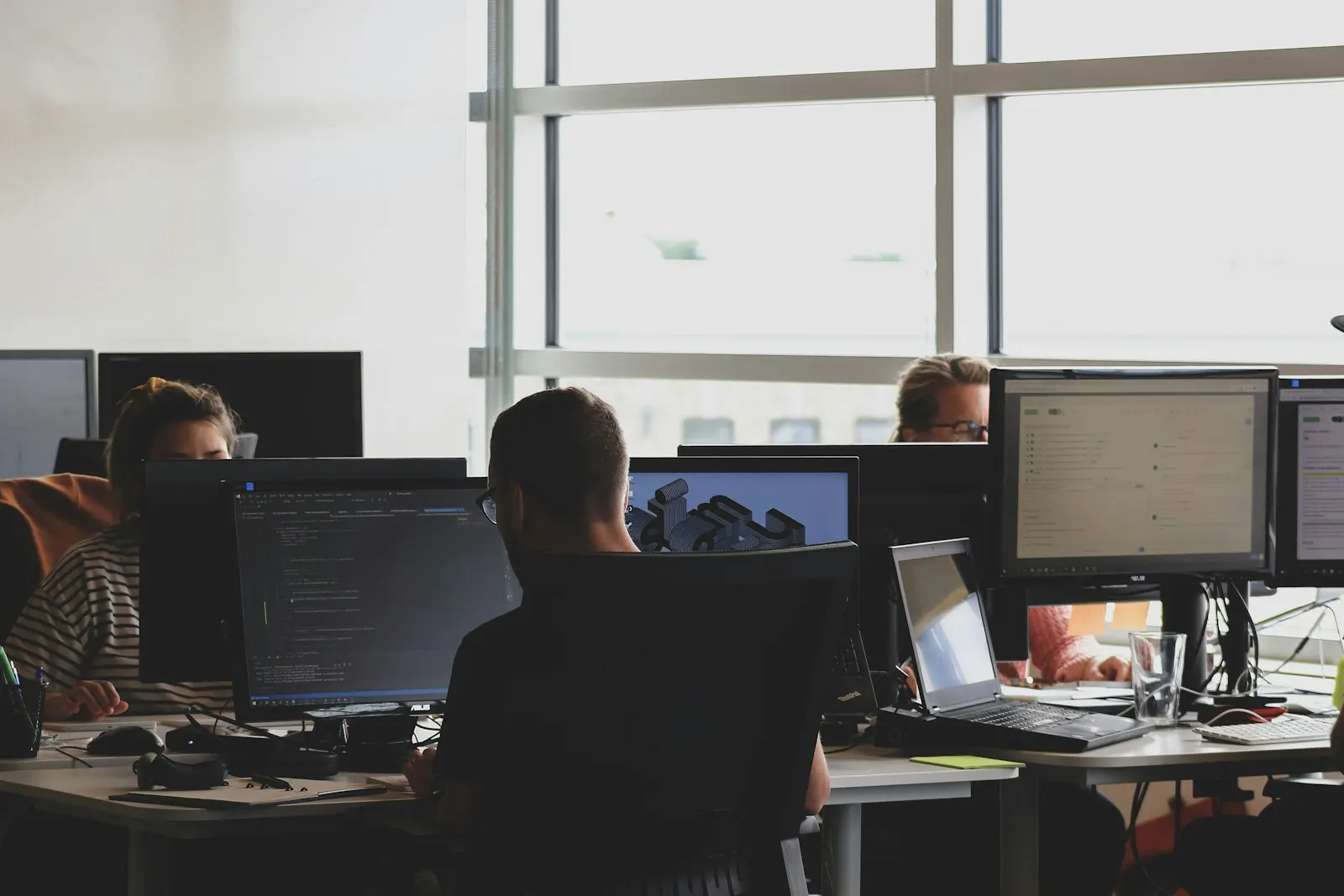 DevOps Engineers work at desks of large monitors in an open office.