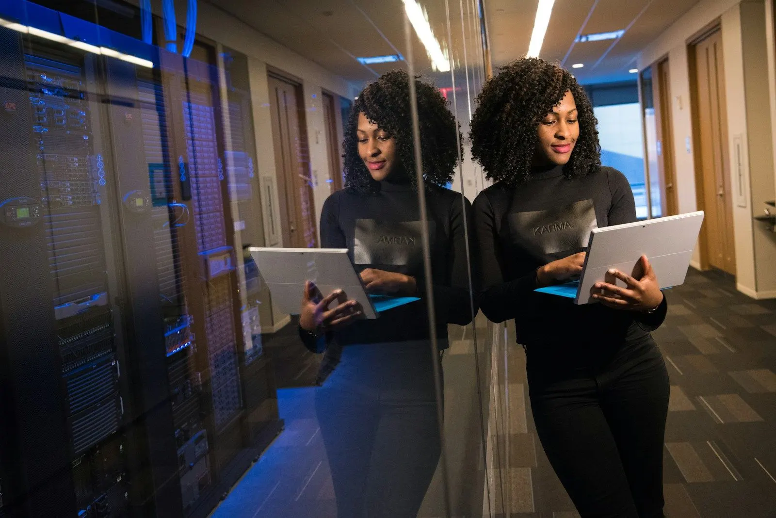 Two platform engineers with tablets talk in a corridor beside server racks.
