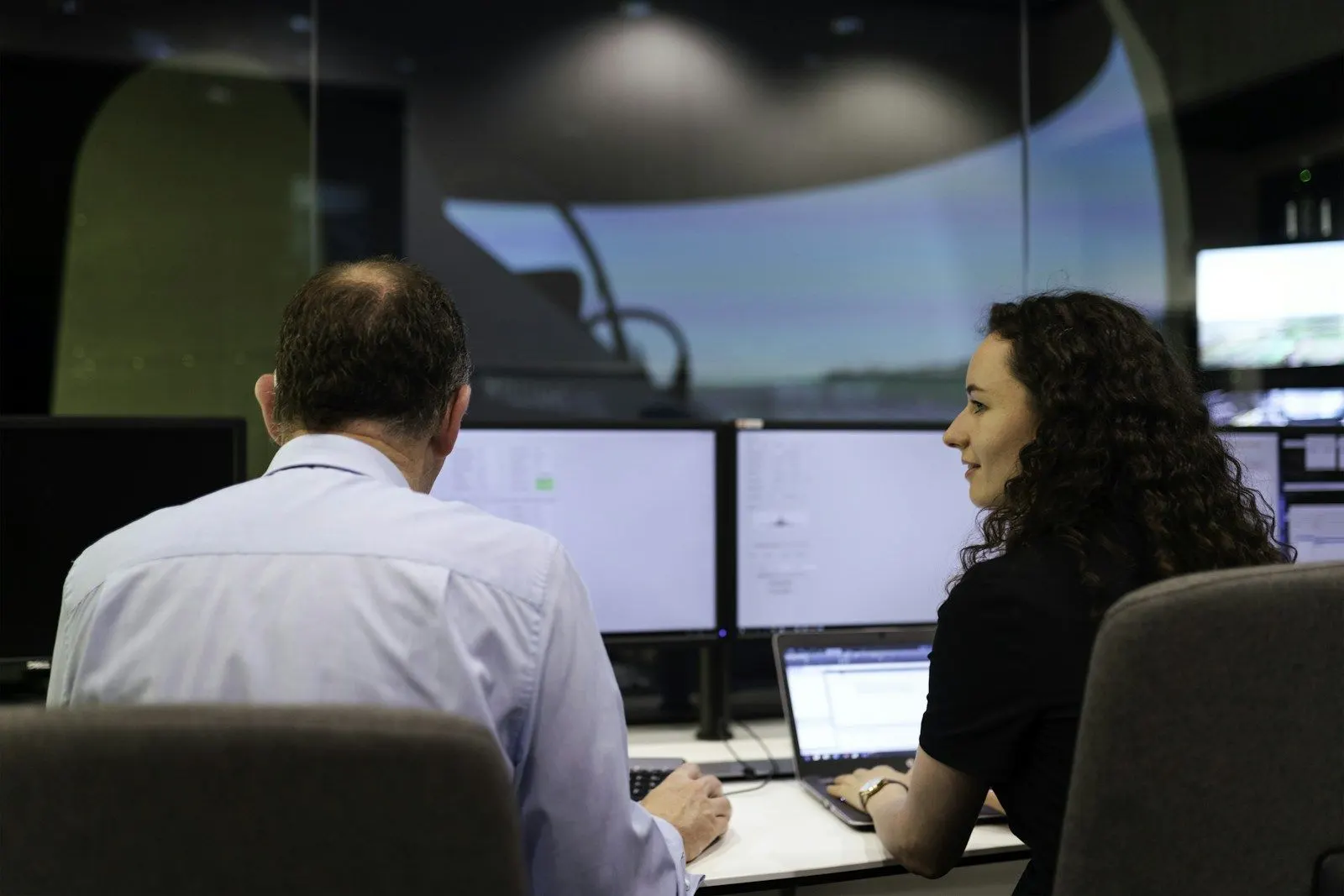 Two DevSecOps engineers work side by side at monitors in an operations room.