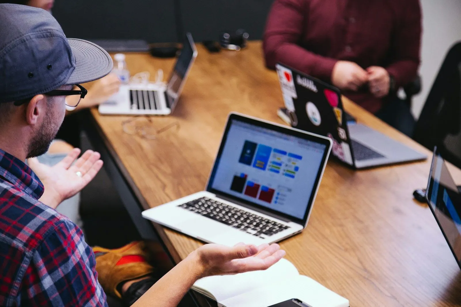 Two DevOps Engineers discuss a project across a table with laptops.
