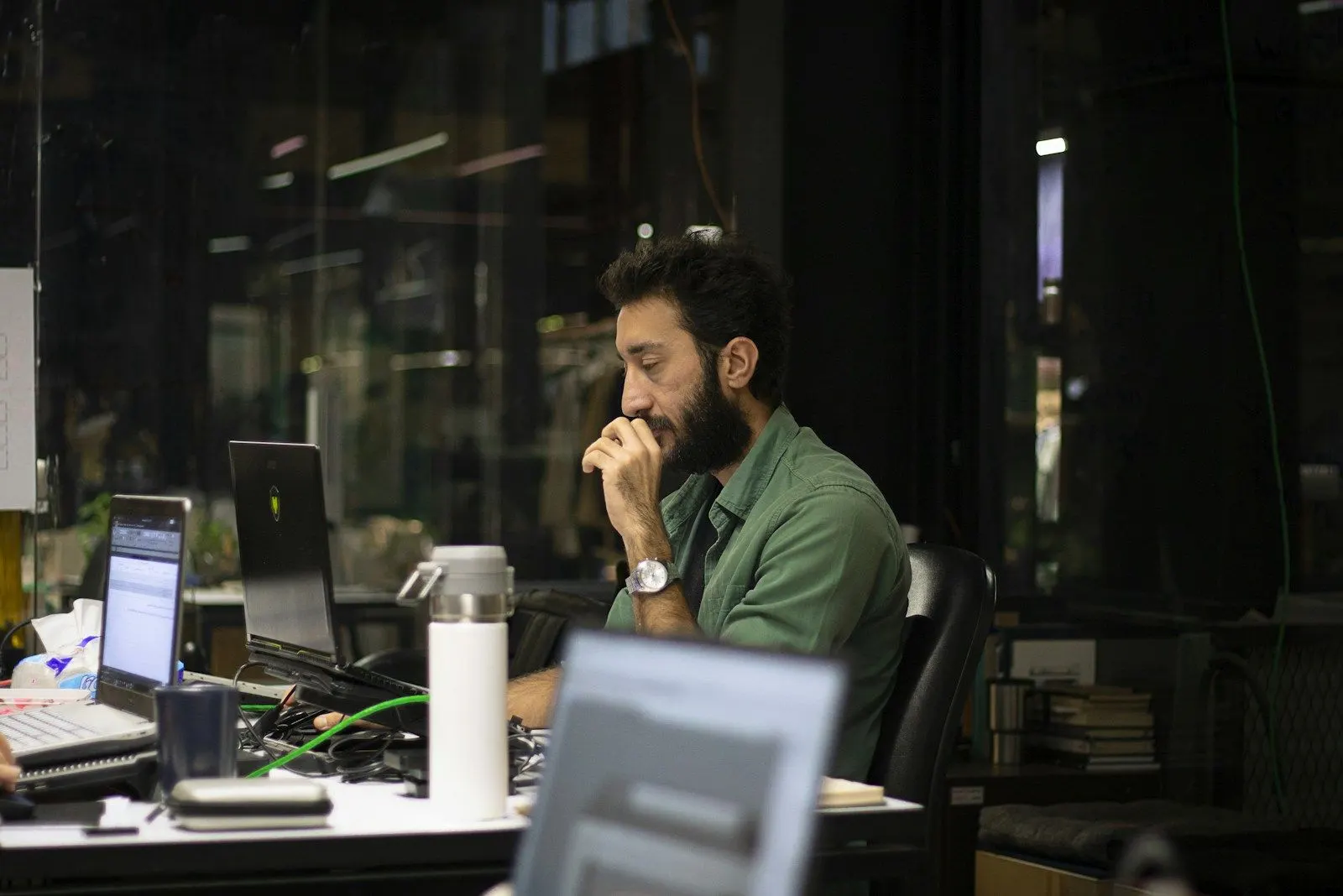 A DevOps engineer in a green shirt works across several screens in a dark office.