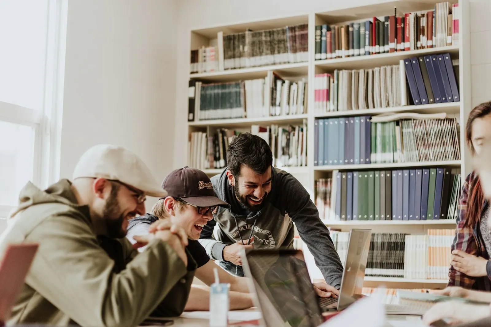 Engineers on an IT staff augmentation engagement laughing together over a laptop in a library-lined studio.