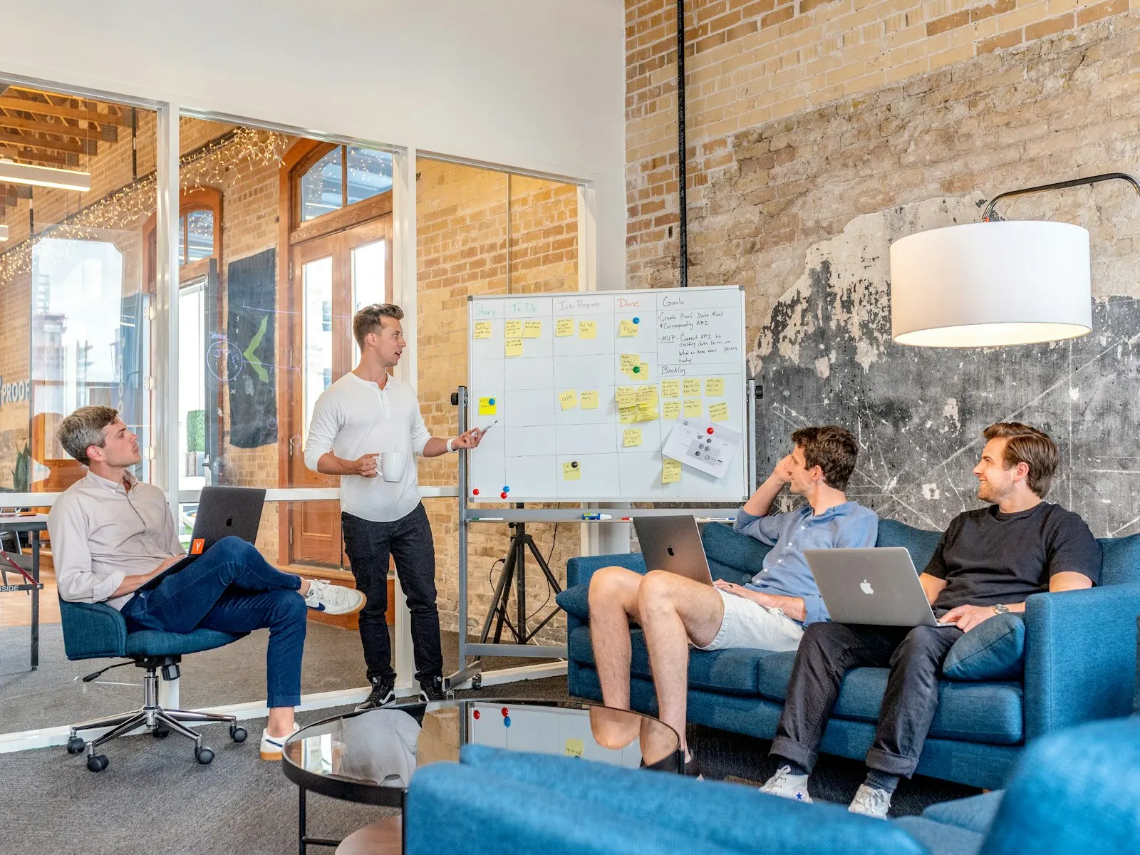 An IT staff augmentation engineer gathering with the client team on sofas, talking through a plan at a whiteboard.
