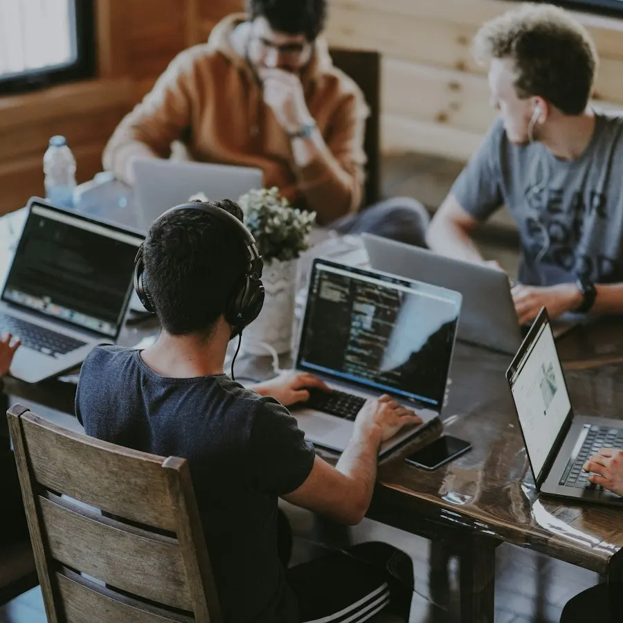 A team of engineers in headphones working at laptops around a shared table
