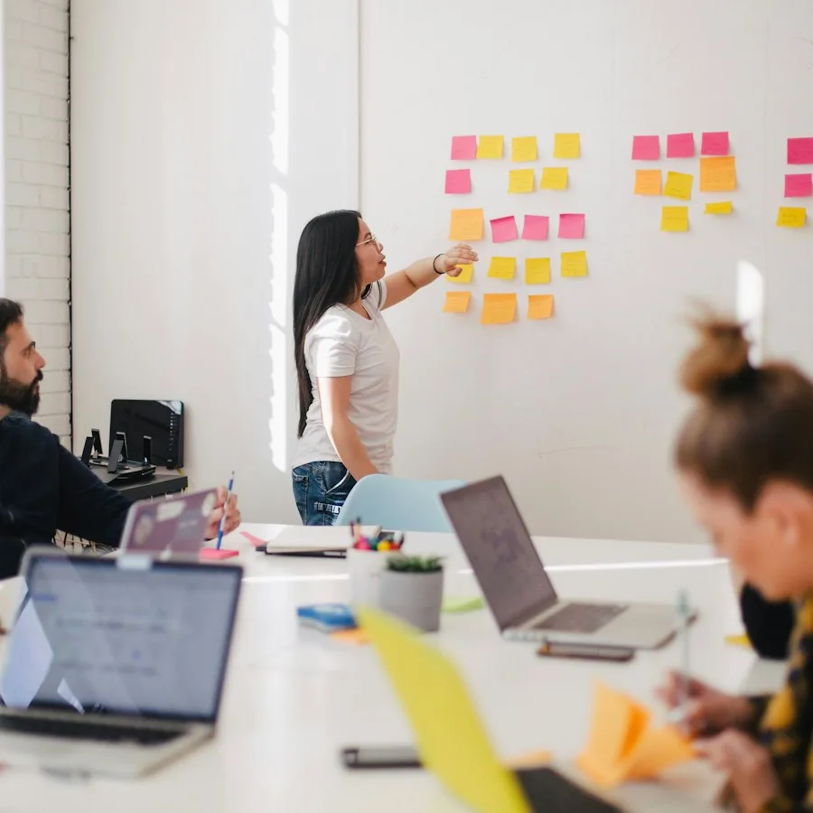 A product lead maps a care workflow on sticky notes while the team works at laptops.